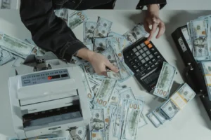 Hands counting hundred-dollar bills with a calculator and money counter on a table