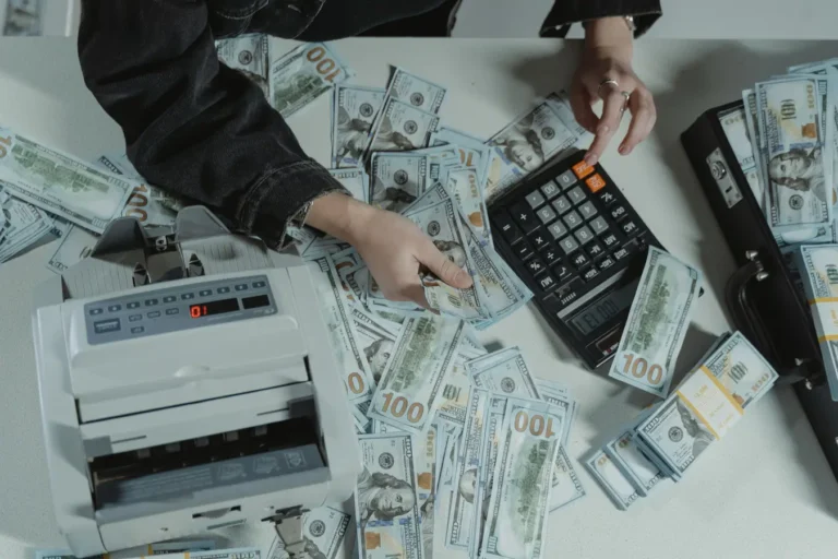 Hands counting hundred-dollar bills with a calculator and money counter on a table