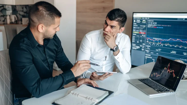 Two businessmen reviewing stock market trends on trading screens in an office
