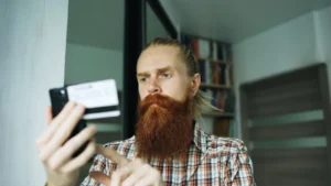 Bearded man shopping online on smartphone with credit card at home