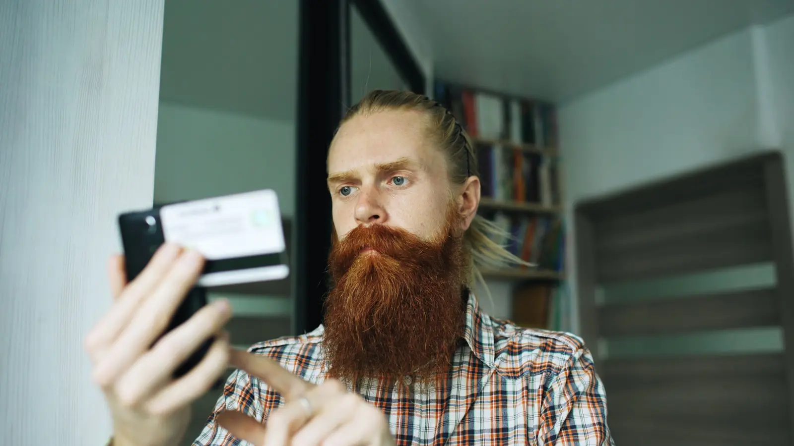 Bearded man shopping online on smartphone with credit card at home