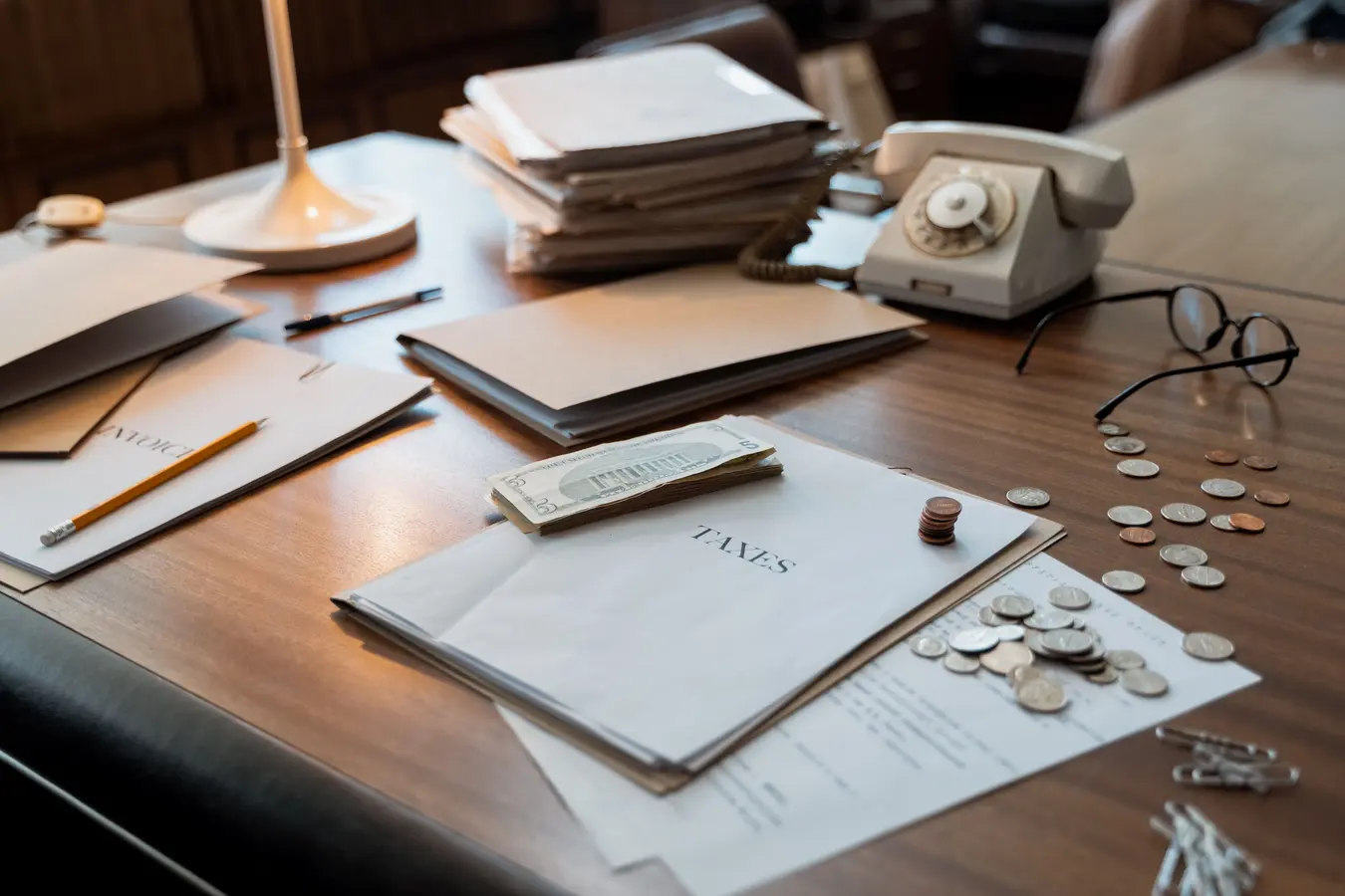 Office desk with tax documents, coins, glasses, and old phone, symbolizing public finance and budgeting
