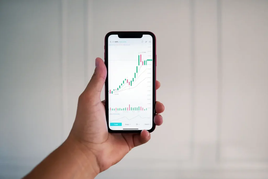 Hand holding a smartphone displaying a forex trading app chart indoors