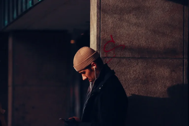 Man in beanie hat with earphones using smartphone against a building wall in Jönköping