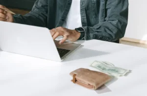 Man using a laptop for online purchases with wallet and cash on the table