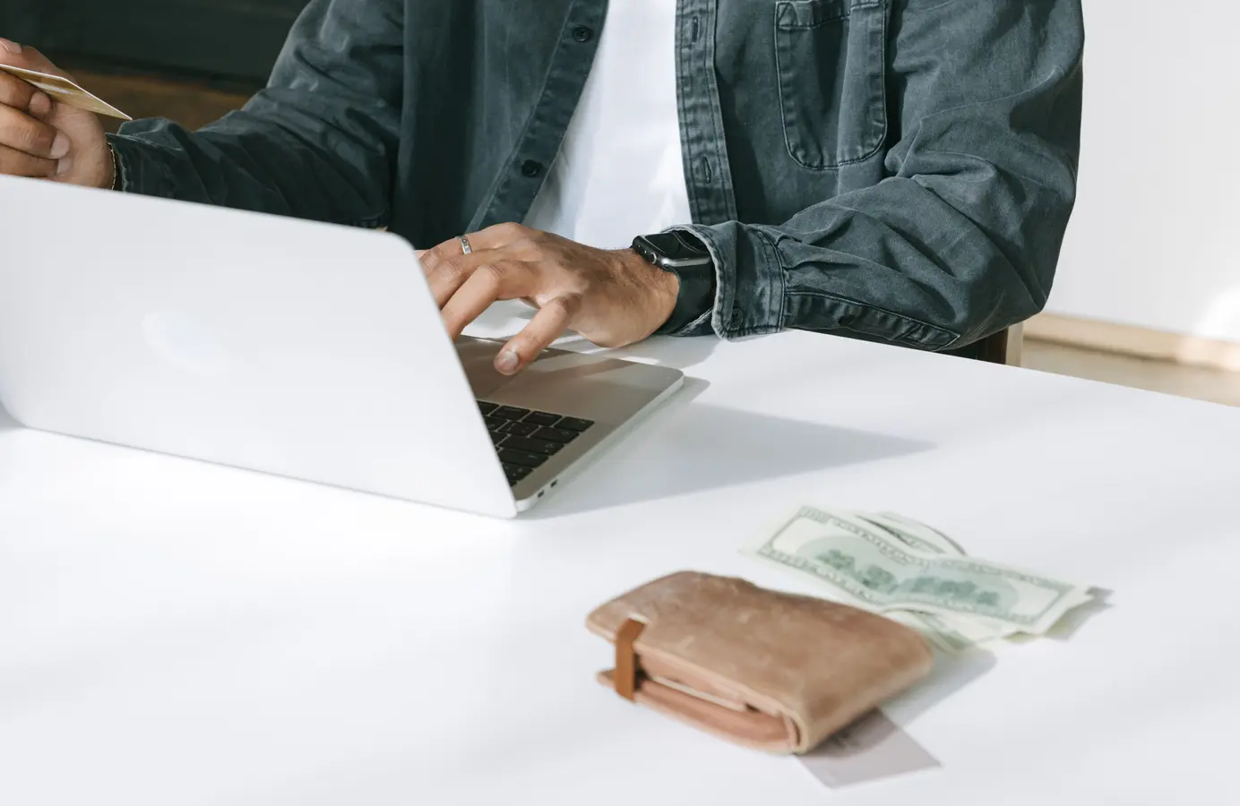 Man using a laptop for online purchases with wallet and cash on the table