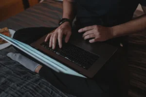 Man sitting cross-legged on bed using laptop, researching password managers for Mac OS X