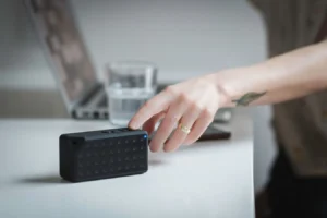 Person adjusting a portable Bose Bluetooth speaker on a desk beside a laptop