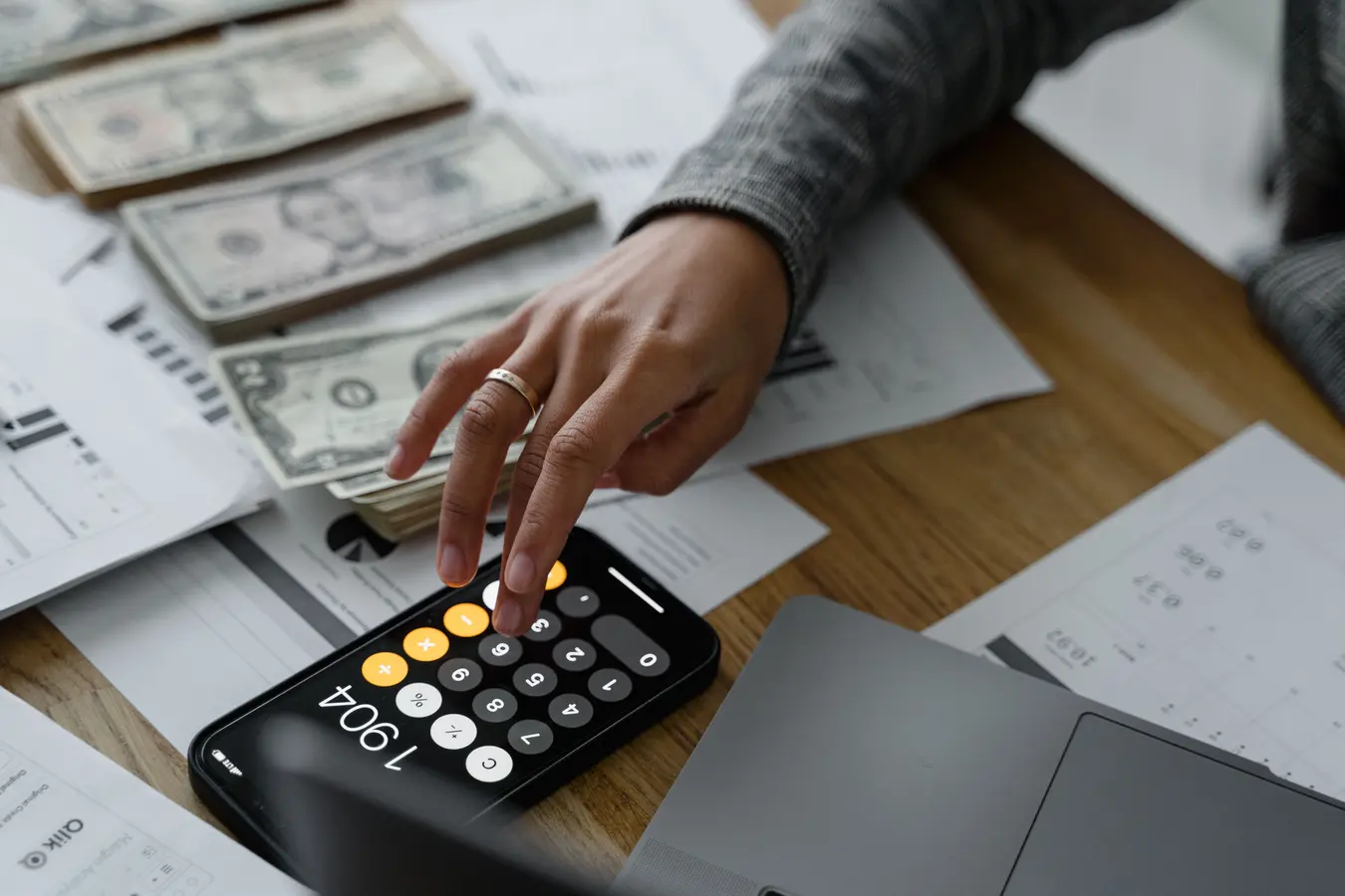 Person using a smartphone calculator with cash and financial documents to calculate high yield savings account earnings