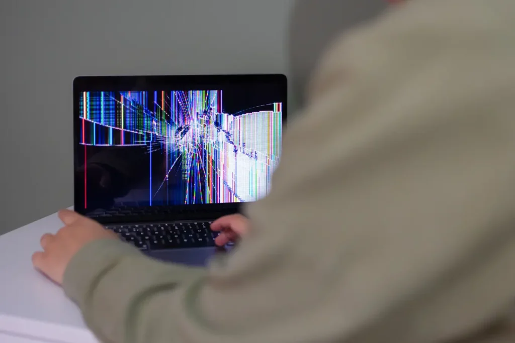 Person using a laptop with a cracked, distorted screen during a Google Password Manager access issue