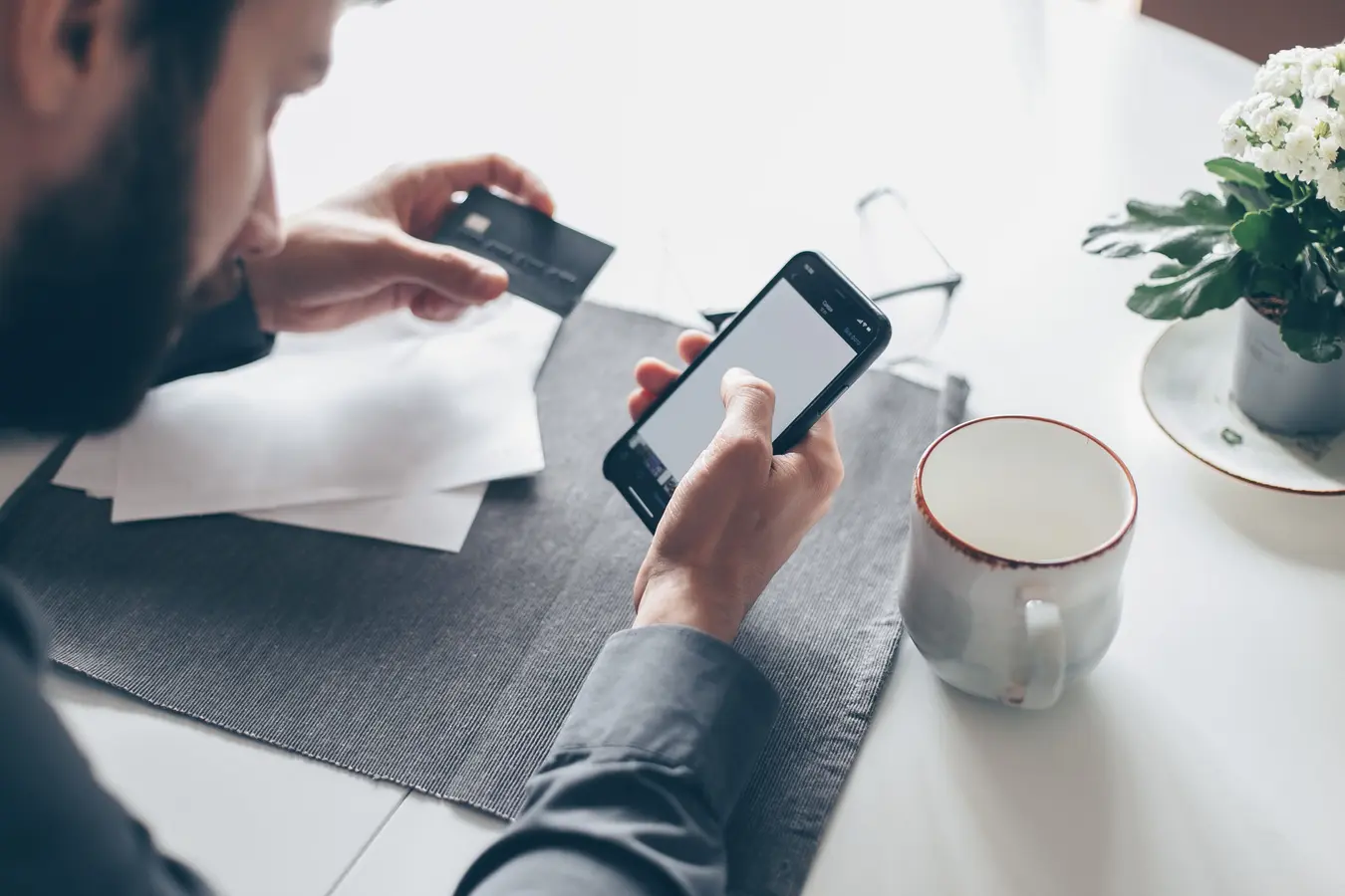 Man using a smartphone and credit card for online banking or payments in soft light
