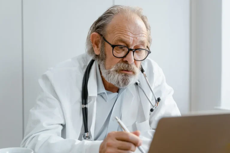 Doctor with glasses and stethoscope working on a laptop in a medical office