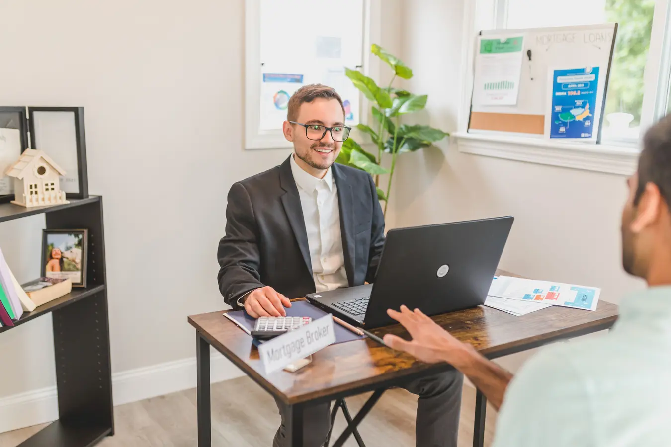 Mortgage broker meeting with a client in an office, discussing an equity mortgage loan on a laptop
