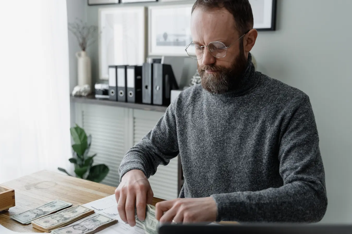 Man in gray sweater counting dollar bills at desk, illustrating Fidelity HSA financial planning