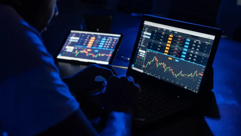 Man analyzing financial charts on laptops in a dim room for forex trading broker research