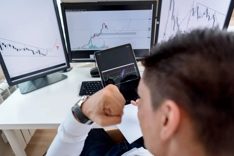 Trader reviewing forex trading charts on multiple monitors in a modern workspace