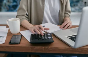 Person using a calculator and laptop while taking notes for a home equity mortgage calculator