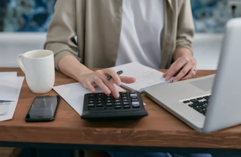 Person using a calculator and laptop while taking notes for a home equity mortgage calculator
