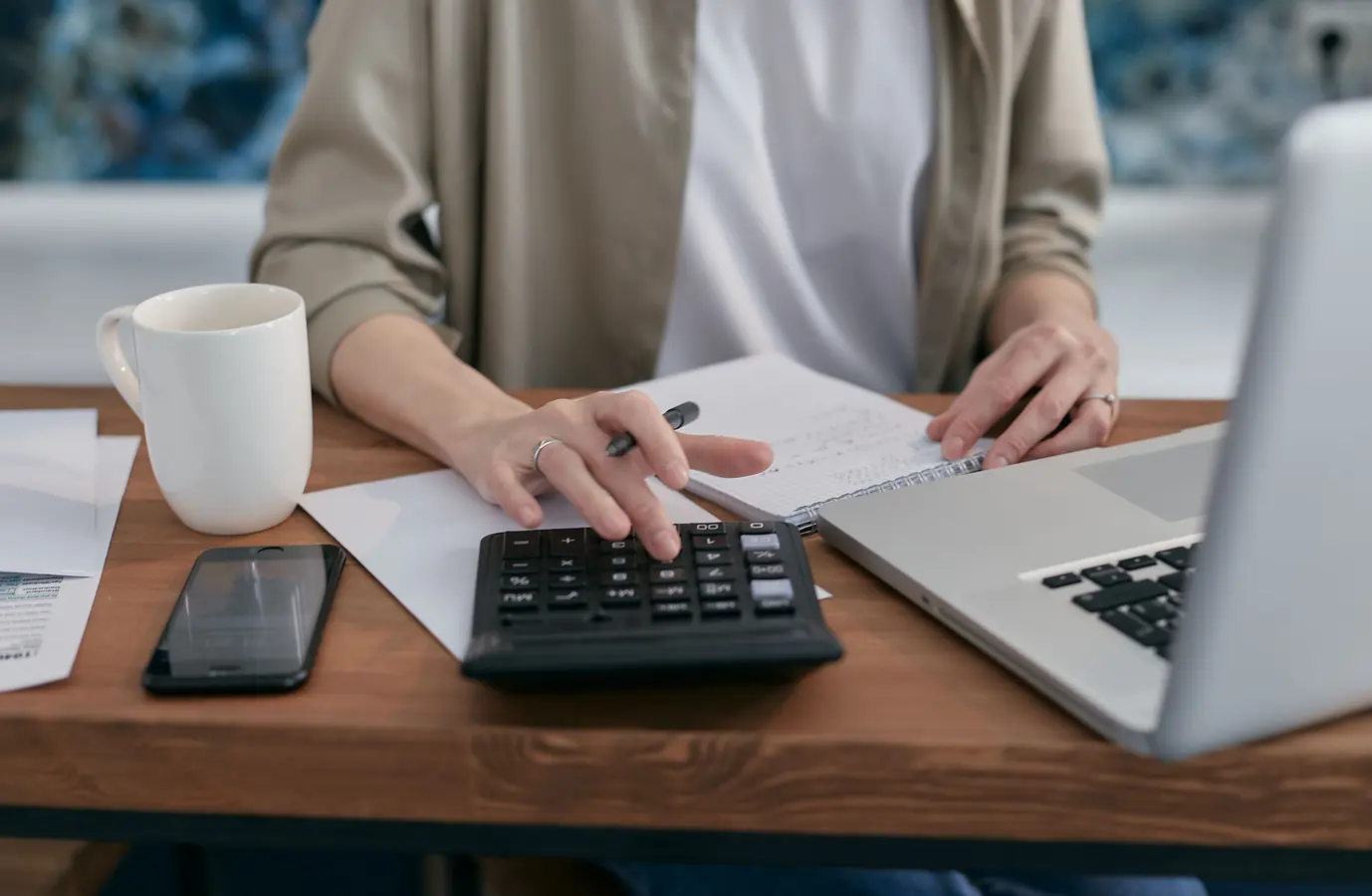 Person using a calculator and laptop while taking notes for a home equity mortgage calculator
