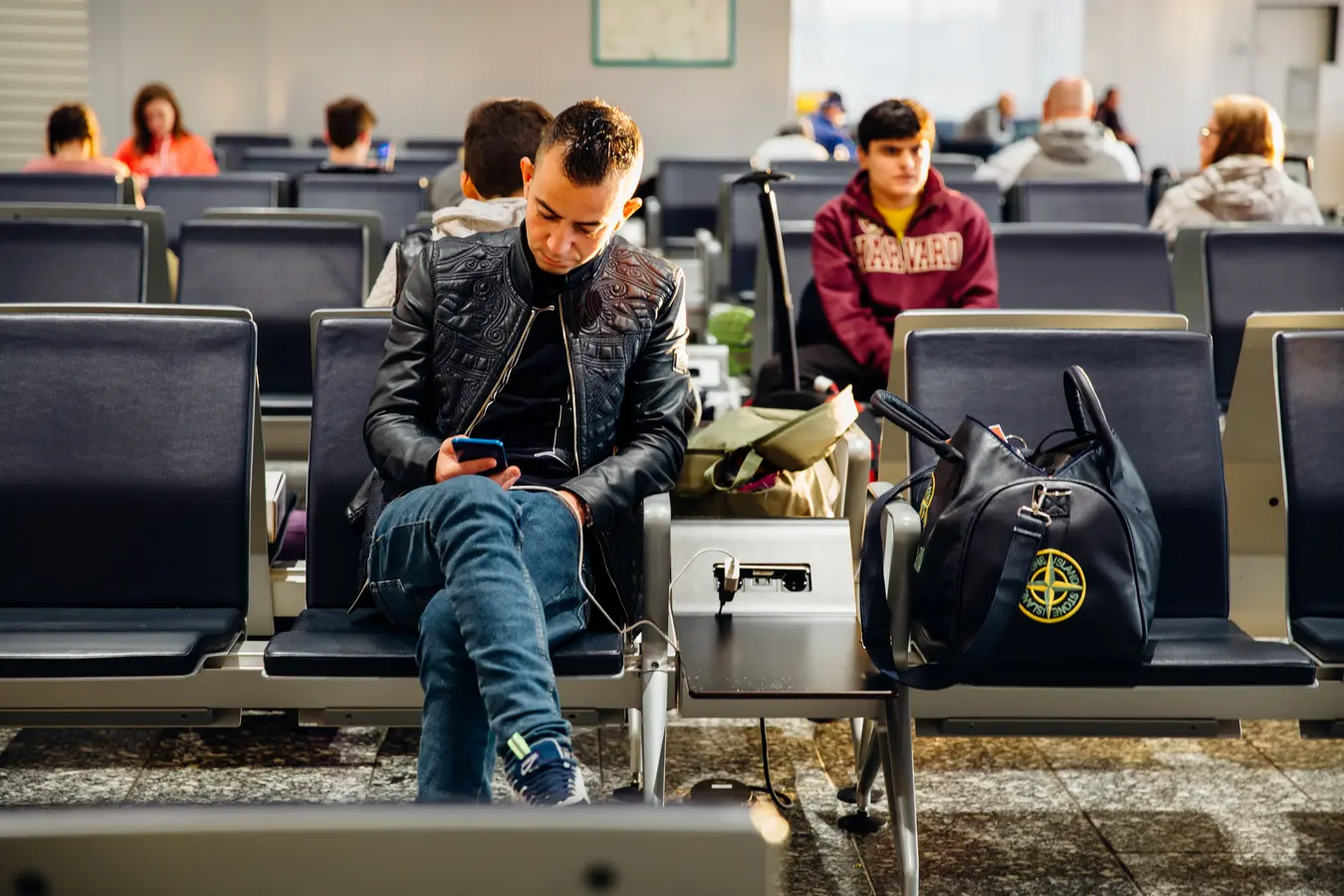 Travelers sitting in an airport lounge using smartphones while waiting for flights