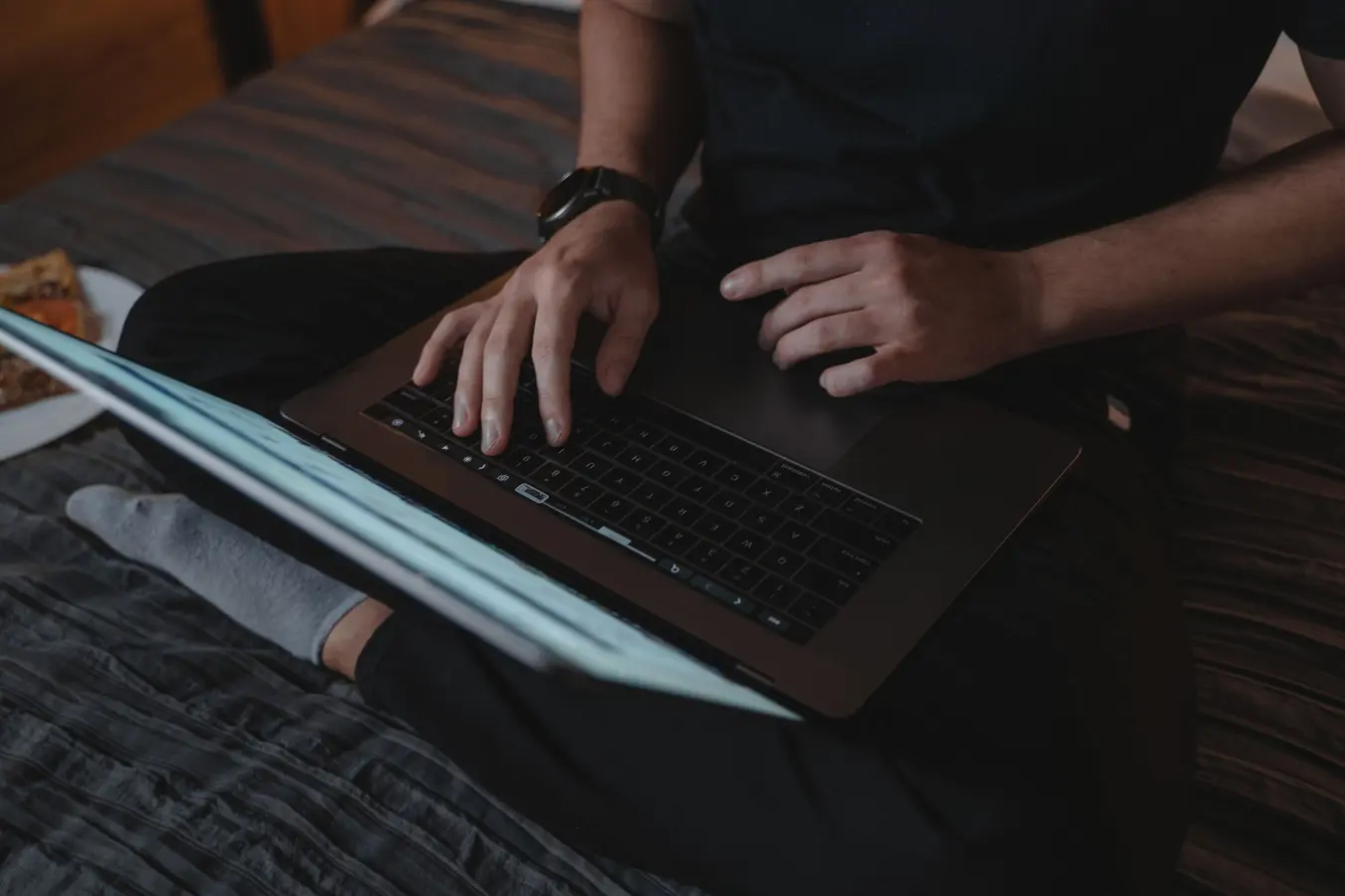 Man sitting cross-legged on bed using laptop indoors, relevant to Chrome password manager safety