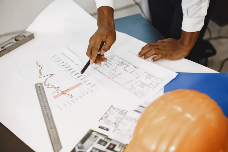 Architect reviewing blueprints and financial charts at a desk for project financing analysis