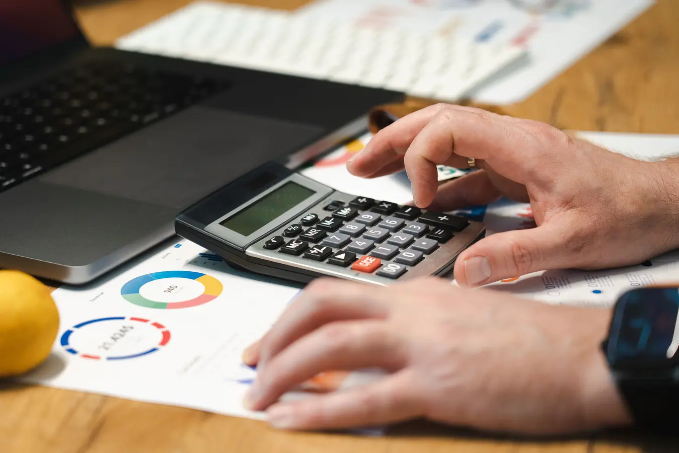 Person using a calculator and laptop to review mortgage payoff and loan costs