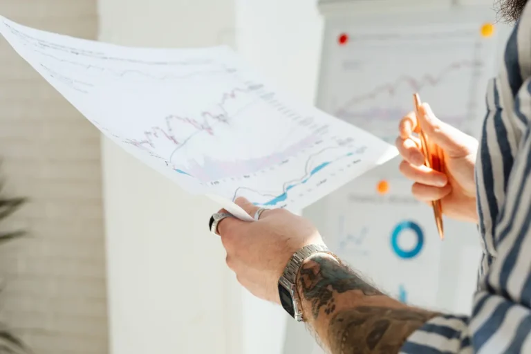 Tattooed hands holding financial charts during stock market data analysis