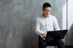 Asian man wearing glasses focused on laptop work in an indoor office setting