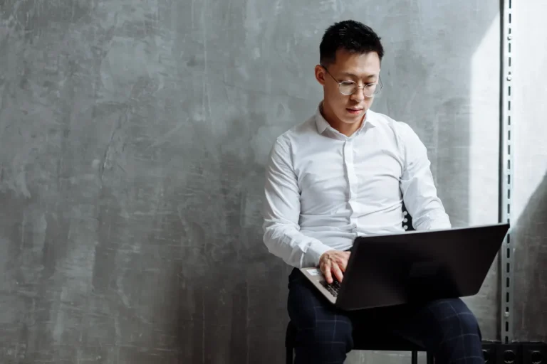 Asian man wearing glasses focused on laptop work in an indoor office setting