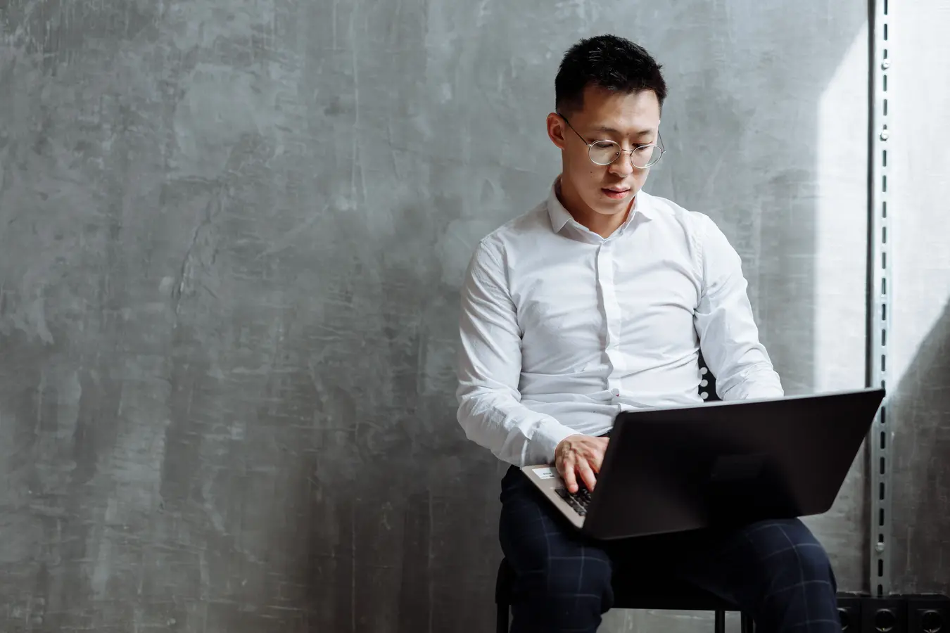 Asian man wearing glasses focused on laptop work in an indoor office setting