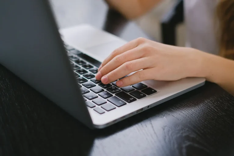 Hand typing on a laptop keyboard on a wooden desk in Opera browser password manager context