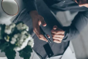 Top view of hands holding an Android smartphone indoors beside a cup and flowers