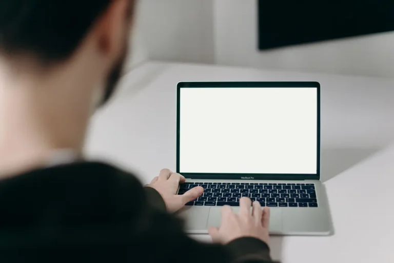 Man in a hoodie using a laptop at a clean, minimalist indoor workspace