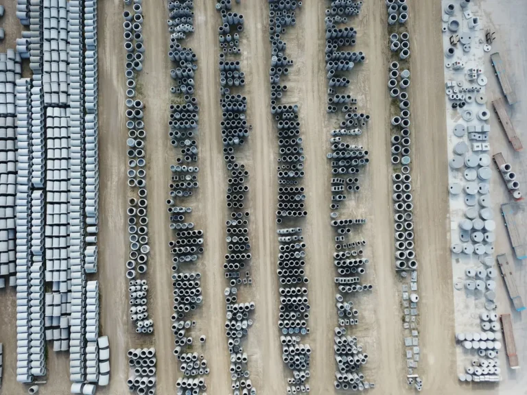 Drone view of an organized outdoor concrete manufacturing facility with stacked pipes and materials