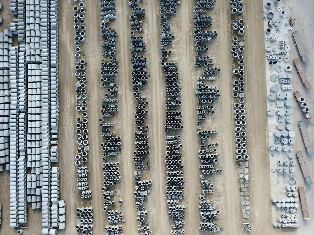 Drone view of an organized outdoor concrete manufacturing facility with stacked pipes and materials
