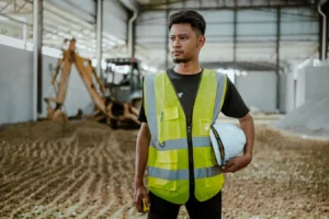 Construction worker in safety gear holding a helmet in an industrial building setting