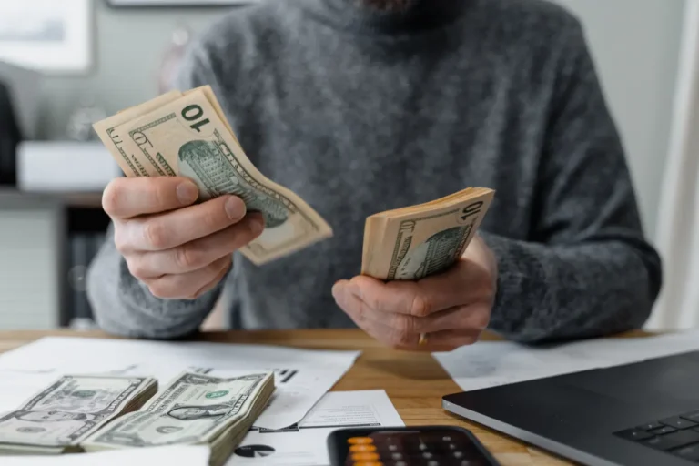 Person counting cash with calculator and paperwork while comparing highest interest rates savings account options