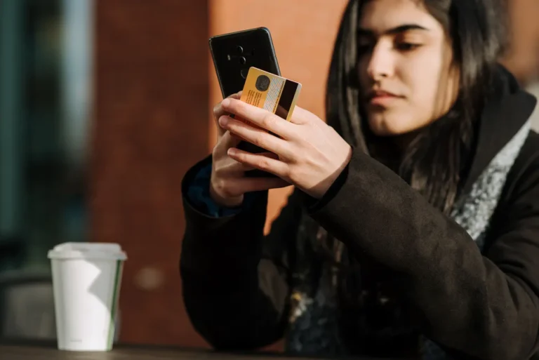 Young woman shopping on her cellphone with a card beside a takeaway drink in a cafeteria