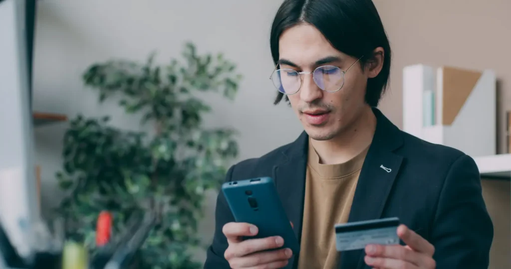 Businessman in office attire using a smartphone and credit card for online account login