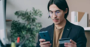 Businessman in office attire using a smartphone and credit card for online account login