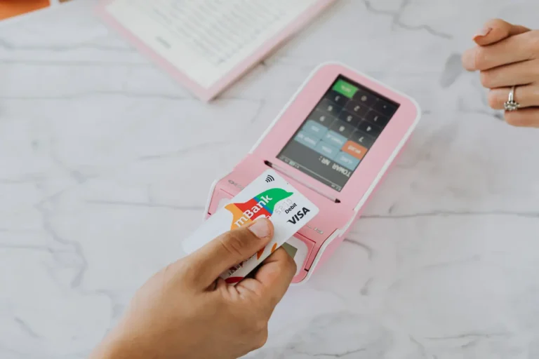 Hand tapping a contactless card on a pink payment terminal during checkout