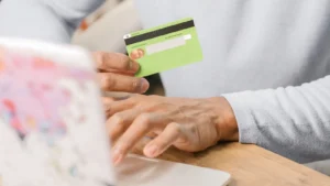 Hands holding a green credit card while shopping online on a laptop