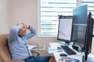 Excited man watching multiple market monitors during active forex trading hours in a modern office