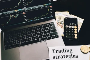 Laptop with market charts, calculator phone, euro bills, coins, and forex trading notes
