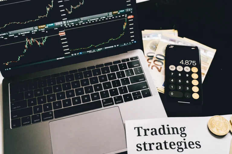 Laptop with market charts, calculator phone, euro bills, coins, and forex trading notes
