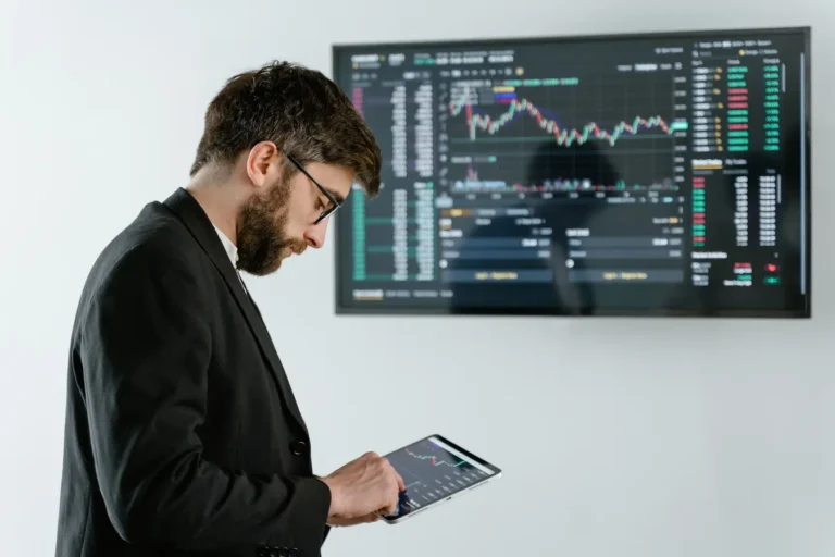 Professional man using a tablet in front of a cryptocurrency trading screen indoors