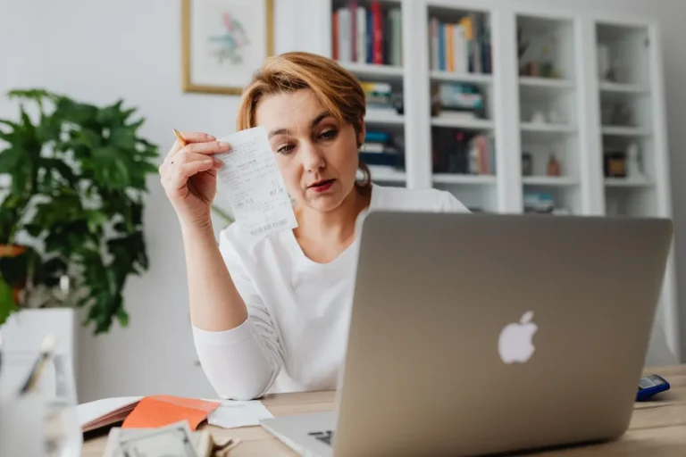 Woman reviewing receipts on a laptop, showing financial stress over savings and account decisions