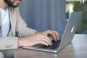 Bearded entrepreneur in a jacket using a modern netbook at a wooden table in daylight