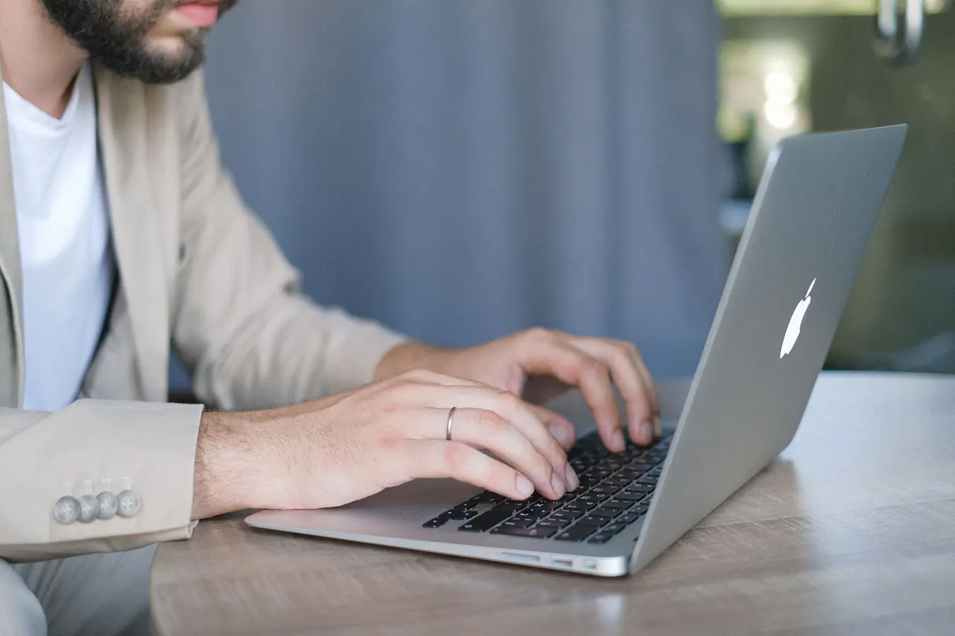 Bearded entrepreneur in a jacket using a modern netbook at a wooden table in daylight